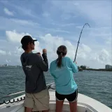 Young angler fighting a fish from the bow of a Sarasota fishing charter boat with a captain providing guidance.