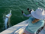 Young angler fishing from the bow of a Sarasota fishing charter boat while a captain records the moment during sunset.