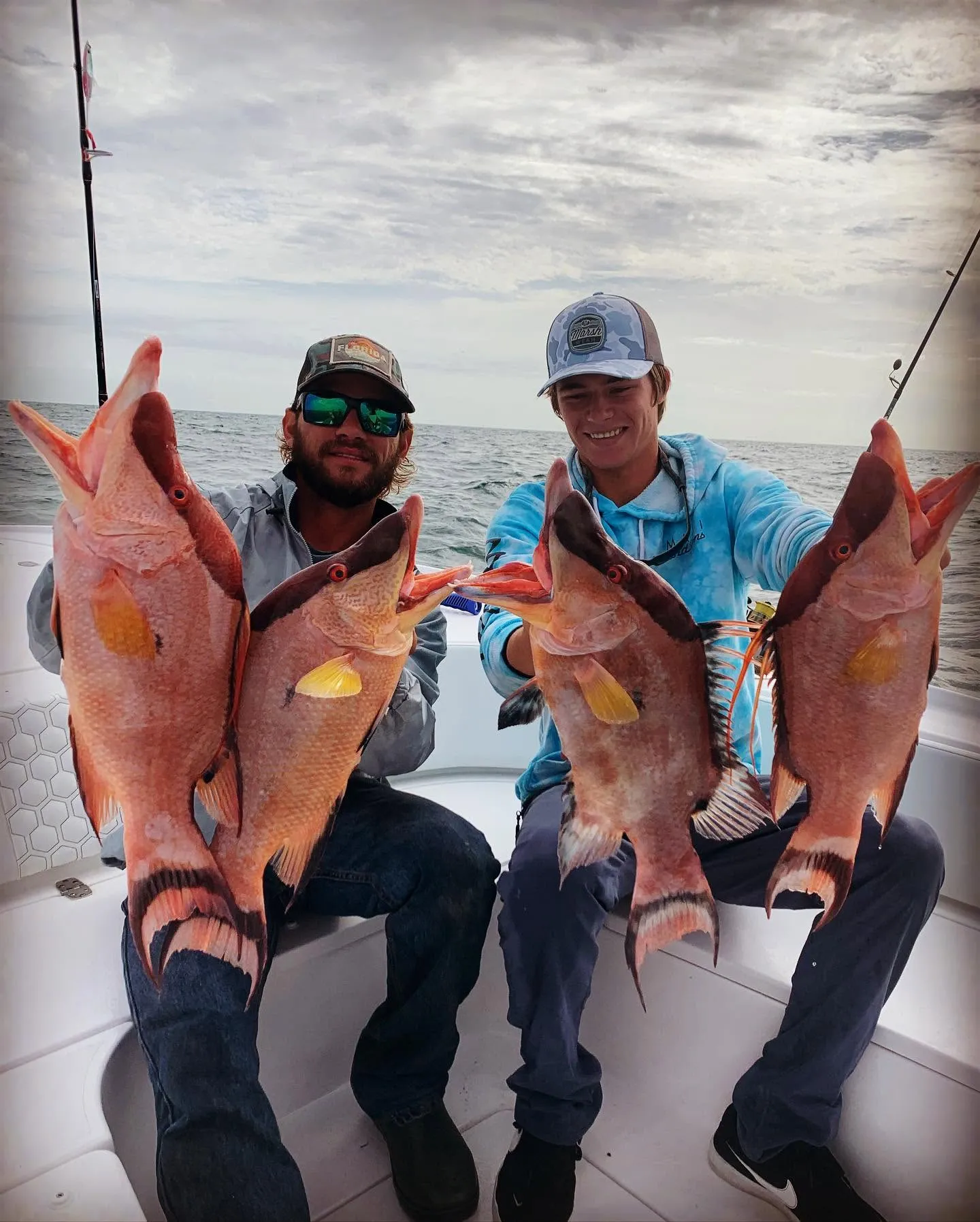 Two anglers holding a mixed catch of vermilion snapper and gray triggerfish during an offshore fishing charter near Sarasota, Florida.