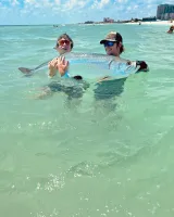 Two young anglers holding a large tarpon in shallow water during a Sarasota fishing charter before releasing the fish.