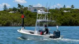 Center console fishing boat cruising through Sarasota Bay with a tower, multiple fishing rods, and two white egrets perched aboard.