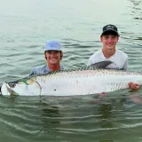 Two anglers holding a large trophy tarpon in the water after a successful catch during a Sarasota fishing charter.
