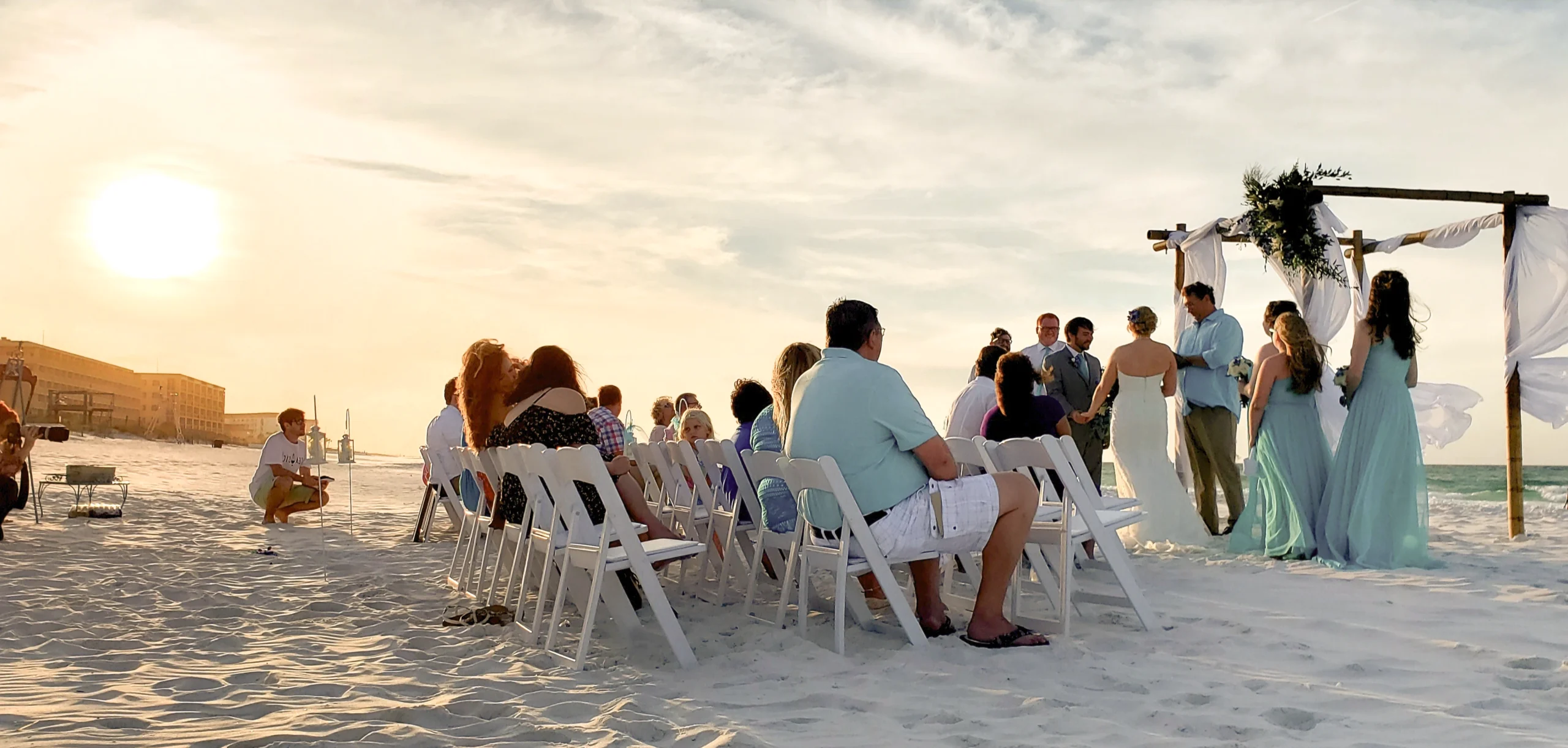 Beachfront wedding ceremony at sunset in Sarasota, Florida with guests seated as the couple exchanges vows beside the Gulf of Mexico.