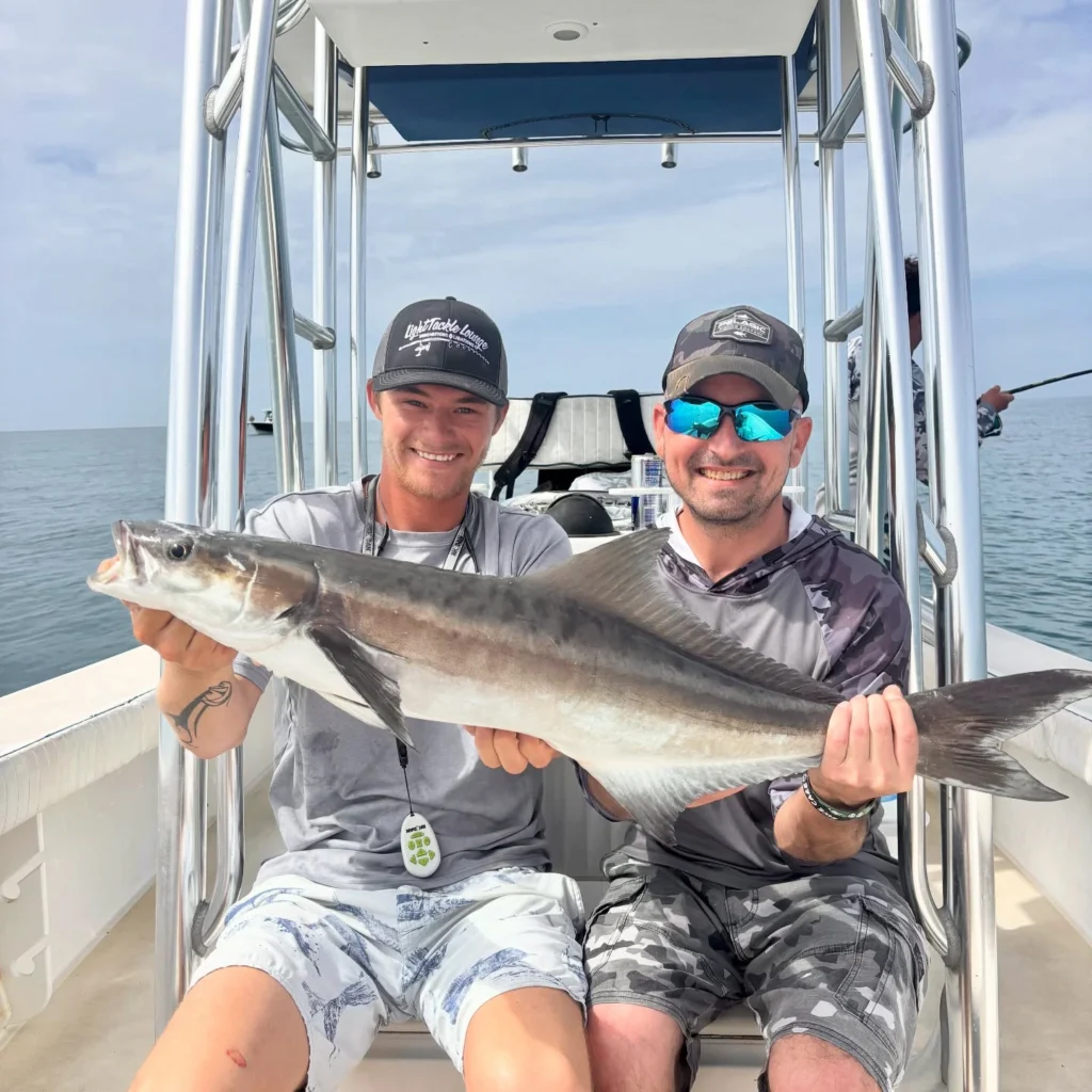 Anglers holding a freshly caught cobia aboard a fly fishing charter boat in Sarasota Bay.