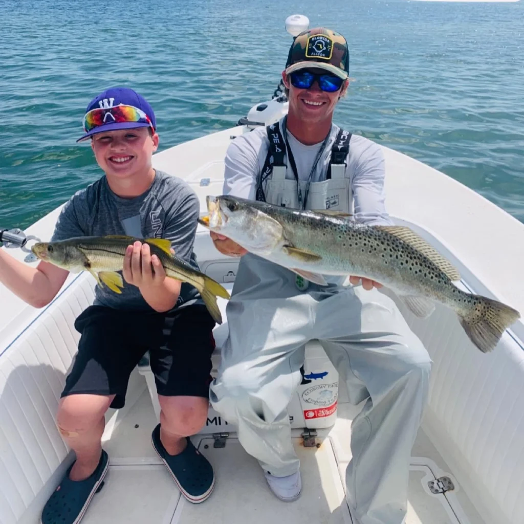 Young angler and captain holding a sea trout and snook during a Sarasota family fishing charter.