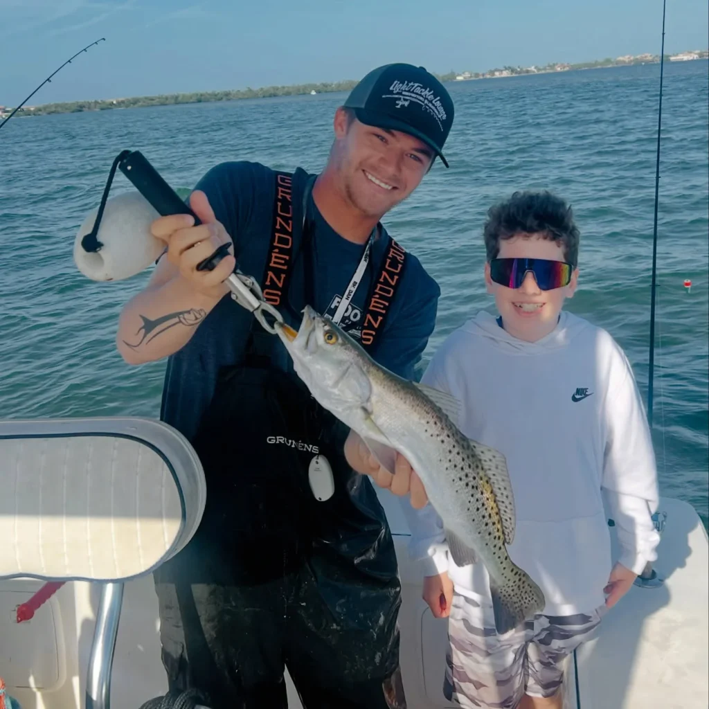 Young angler and captain holding a speckled sea trout during a Sarasota family fishing charter.