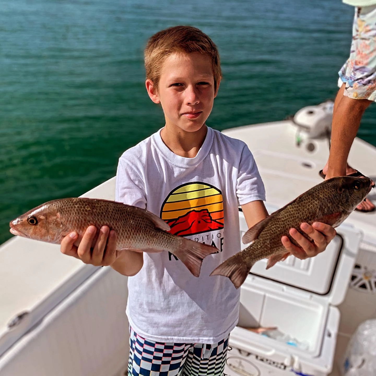 Young angler holding two redfish during a Sarasota family fishing charter.