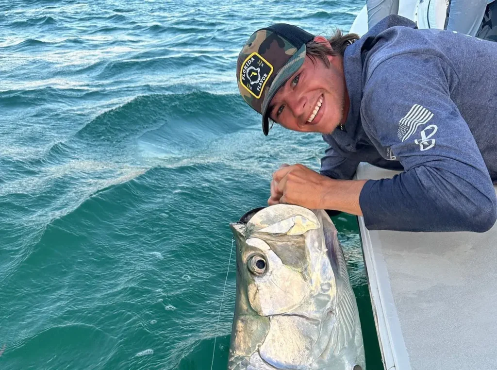 Captain Kyle holding a large tarpon beside the boat during a Sarasota fishing charter.