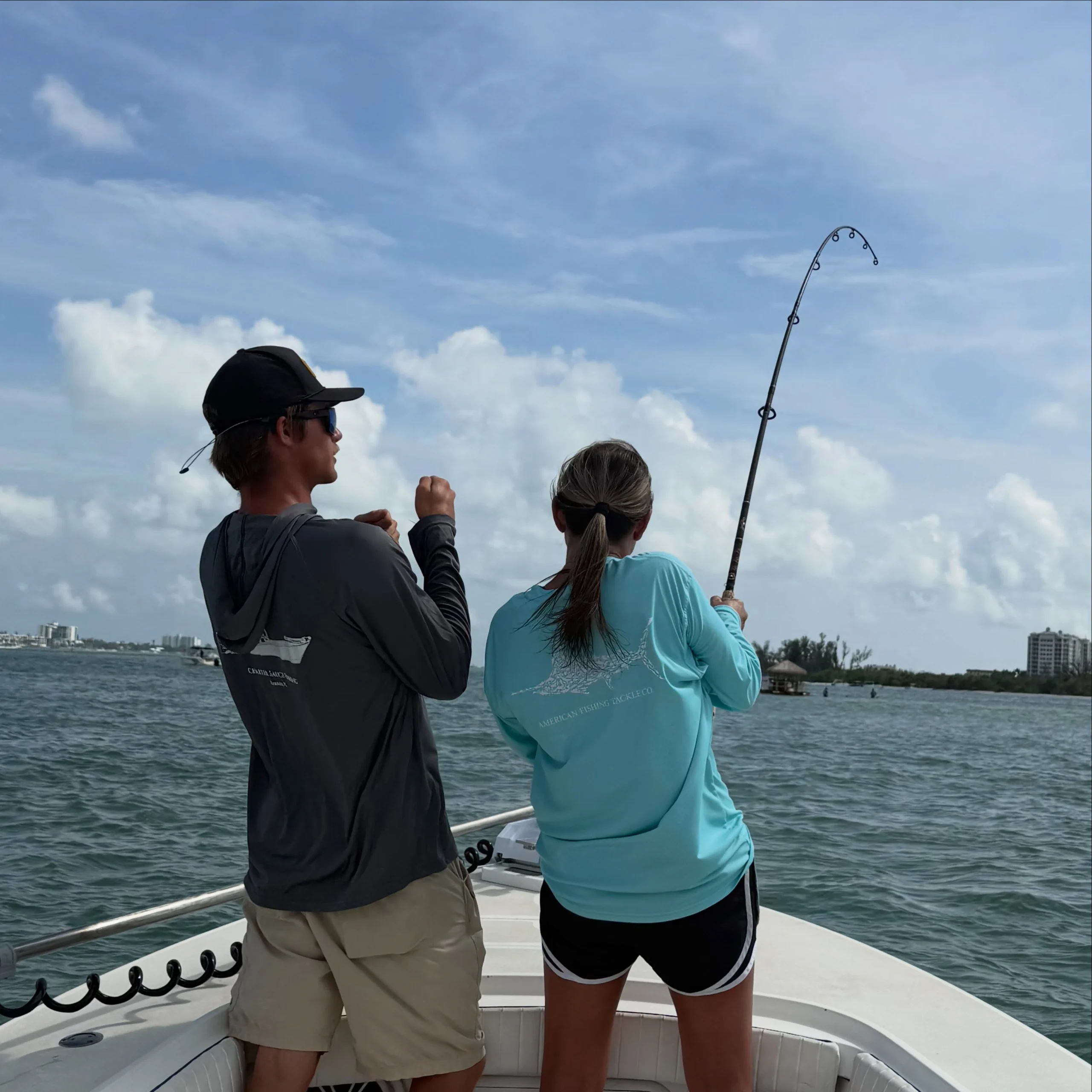 Young angler fighting a fish from the bow of a Sarasota fishing charter boat with a captain providing guidance.