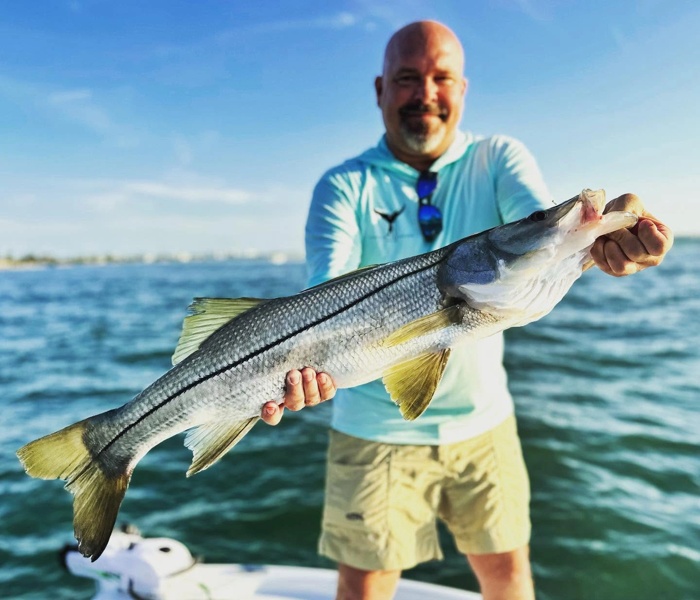 Angler holding a large snook aboard a Sarasota fishing charter boat on calm inshore waters.