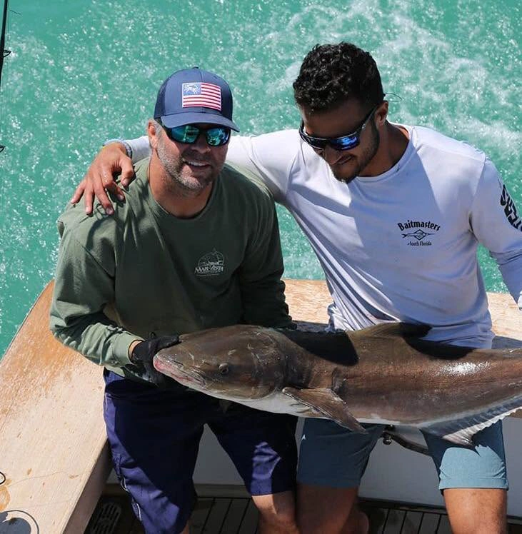 Two anglers holding a juvenile goliath grouper during an offshore fishing charter in the Gulf of Mexico near Sarasota, Florida.
