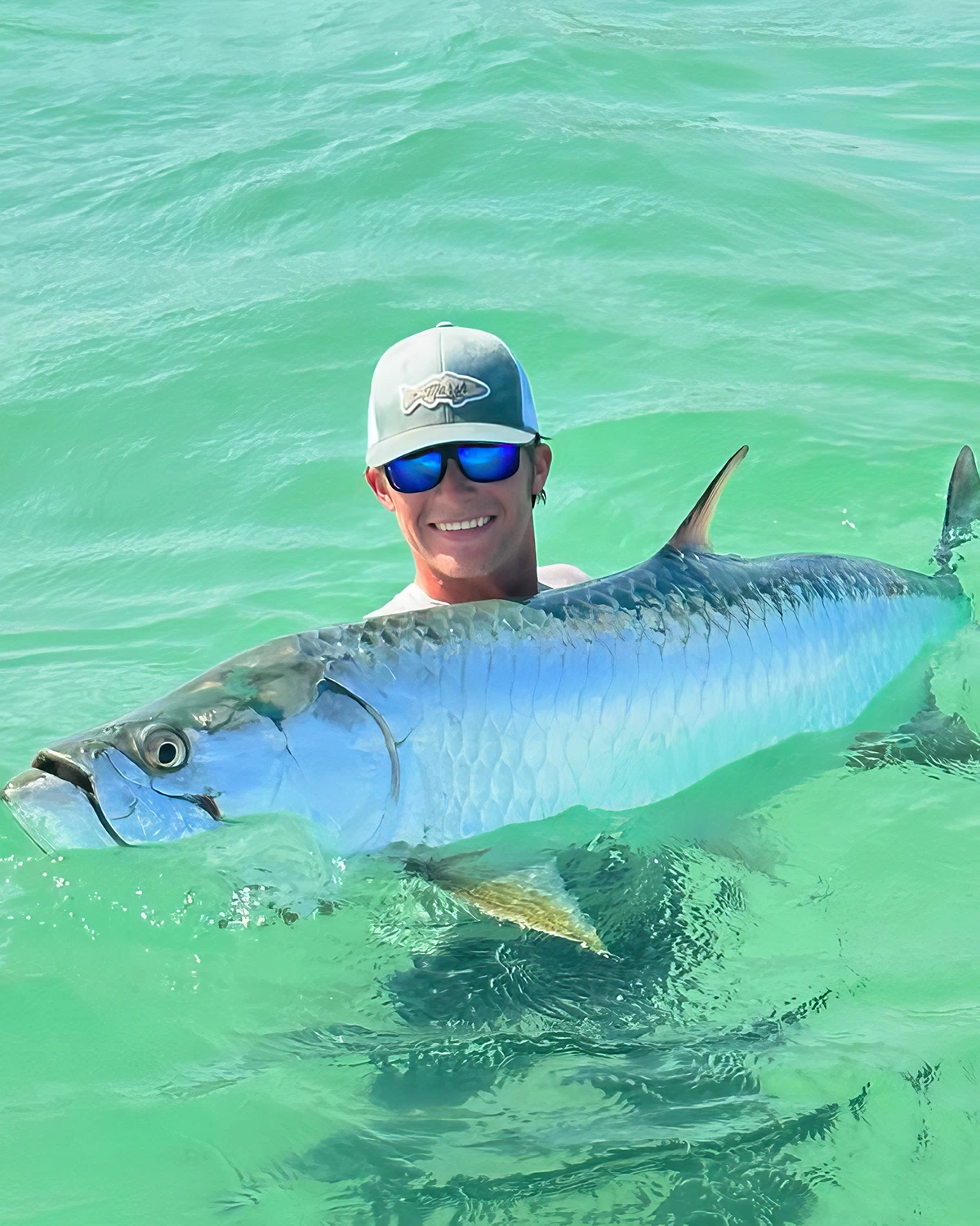Angler holding a healthy silver tarpon in the clear waters of Sarasota Bay during a catch-and-release fishing charter.