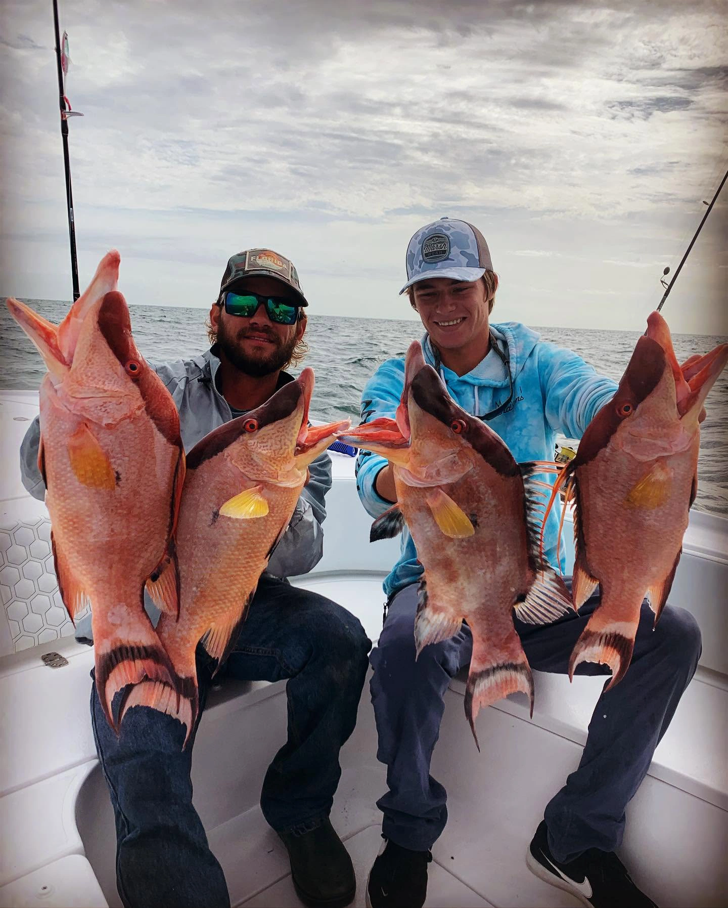 Two anglers holding a mixed catch of vermilion snapper and gray triggerfish during an offshore fishing charter near Sarasota, Florida.
